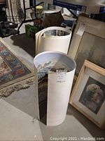 Rolled posters standing on floor of basement; partially visible winter scene print shows detailed landscape with mountains and trees.