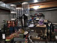 Wide shot showing multiple kitchen items including canisters, small pots, bowls, French press, electric juicer, and copper pots.
