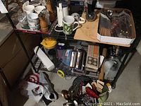 Wide view of kitchen items on metal cart including cups, grinders, tray, utensils, and small appliances.