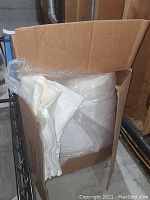 Open cardboard box containing white bedding items such as sheets or pillowcases.