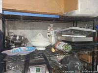 Photo of items on metal shelf: decorative bottles, ceramic dish, platter, broiler pans, bowls, garnishing set.