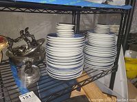 Multiple stacks of various sized ceramic plates and a metal fondue set on a shelf.