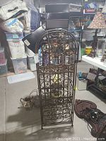 Front view of the metal wine rack showing height and decorative scrollwork with a lock on the door