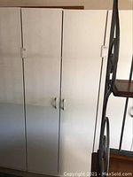 Two tall white melamine storage cabinets side by side with closed doors and handles visible.