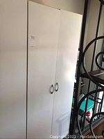 Closed view of one white melamine storage cabinet with two doors and metal handles