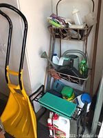 Photo showing the metal garden rack with contents including yellow snow shovel, cushioned bench, watering can, bottles, and containers.