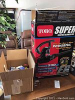 Wide view of the Toro Super Electric Blower Vac box next to a cardboard box containing paint supplies on a wooden surface.