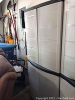 Two tall beige plastic storage cabinets side by side in a garage, showing exterior of doors and black trim.
