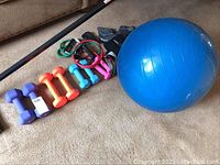Photo showing dumbbells, resistance bands, arm/ankle weights, and blue exercise ball on carpeted floor