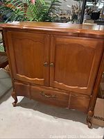 Front view of vintage wood cabinet showing two paneled doors with ornate round metal handles and a single drawer with decorative metal handle at the bottom.