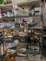 Metal shelving rack with multiple rows of varied painter's tools including brushes, paints, brushes in containers, and storage boxes filled with supplies.