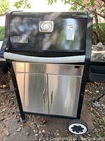 Front view of black and stainless steel Weber gas grill showing grill lid with thermometer and storage cabinet below.
