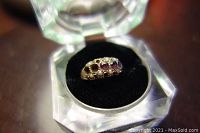 Front view of ring in display case showing three round red stones and two empty settings