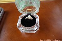 Close-up view of sterling silver ring with triplet opal stone and small white stones, displayed in clear faceted box on brown surface.