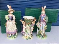 Front view of three Fitz & Floyd Easter bunny figurines and basket vase with green branded boxes in background