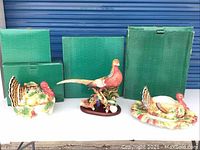 Photo showing three Fitz & Floyd ceramic items (turkey covered dish, pheasant figurine, pheasant platter) in front of green boxes