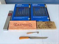 Photo showing two Wiltshire 5-piece kitchen knife sets in their original blue boxes with magnetic racks, several wooden boxed items including Arvers, and carving tools with wooden handles.