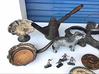 Photo showing various metal decorative items including watering can, metal dog figurines, and silver plates.