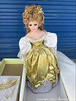 Close-up of one Eaton Beauty Doll showing detailed curly blonde hair, floral hair decorations, pearl necklace, and ornate gold and white gown with puffed sleeves.