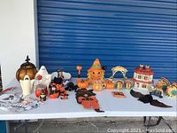 Full view of the Halloween decoration lot including various ceramic ghost figurines, pumpkins, figurines of witches and cats, skeleton mat, and other items arranged on white table.