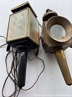 Pair of antique brass lanterns, one converted to electric, laying on flat surface with attached cords visible.