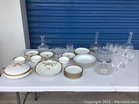 Photo showing the entire set of porcelain and glassware items arranged on a table including platters, plates, glasses, decanters, and bowls.