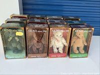 Nine Gund bears in original boxes displayed in 3 rows, showing green, brown, pink, and dark green themed packaging, each labeled with years from 1990 to 2001.