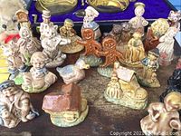 Photo of a assortment of various small ceramic figurines depicting humans, animals, two gingerbread men, and small buildings, displayed on a wooden surface.