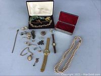 Full view of lot items arranged on table showing watches, pearl necklace, brooches, earrings, bracelet, and cufflinks