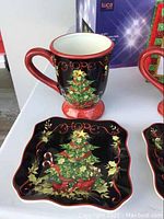 Photo showing a black ceramic mug with a Christmas tree design and the word 'Hope' paired with a matching square plate.