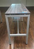 Photo showing side view of long rectangular conference desk with woodgrain surface and silver metal legs on a wooden floor.