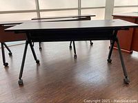 Side view of a rolling office desk with black metal legs and caster wheels on wooden floor.