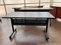 Front view of rolling desk showing wood veneer top and black metal legs with caster wheels