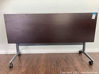 Front view of the brown wood veneer rolling desk showing full length and height with caster wheels visible.