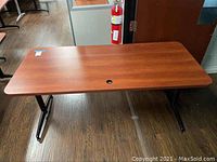 Full view of the large rectangular wooden desk showing smooth top surface, rounded edges, black metal legs, and wire hole near one side.