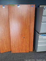 Three standing cubical desktop panels with wood grain laminate and black edge trim. One panel has a circular cutout for cables, indicating use as partition or desk panel.