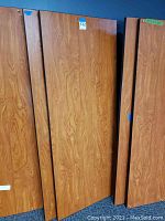 Three brown wood grain laminate desktop panels stacked vertically against a wall, showing the flat surfaces and edges.