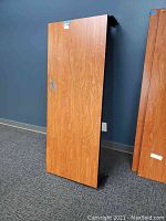 Photo of one wood laminate cubicle desktop upright showing wood grain finish and wall behind.