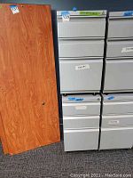 Gray multi-drawer metal filing cabinet with labels and wood panel door next to it.
