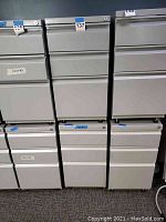 Front view of several metal file cabinets including lot 137, showing the light gray color and drawer layout.