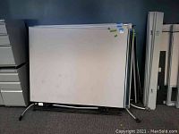 Two rectangular cubical panels stacked against a wall, showing their white surfaces and metallic frame edges.