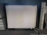 Photo showing a large white cubical office panel with power components visible at the bottom edge, cords trailing to the floor.