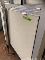 Photo of metal and fabric cubicle partition panels leaning against a wall with visible labeling and measurements