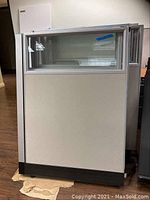 Front view of a metal and fabric office cubicle partition section, showing fabric covered lower panel with upper glass window panel inside a metal frame.