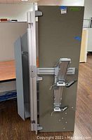 Silver adjustable dual monitor mount shown from side angle attached to vertical panel.