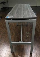 Photo showing close-up of wood laminate top with gray grain and silver metal frame leg structure