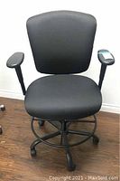 Front view of a black adjustable office chair showing seat, backrest, armrests, foot ring, and wheels.