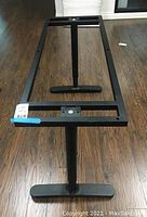 Full view of the black metal rectangular table frame showing two support legs and mounting points for tabletop attachment on wood floor.