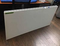 Two white rectangular tabletops leaning vertically against a wall on hardwood floor.