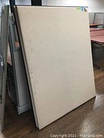Photo of two beige office cubicle partition panels stacked against a wall in an office setting showing front surface and profile.